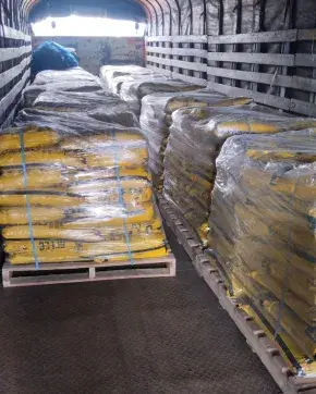 Bultos de cemento conductivo empacados en bolsas amarillas, organizados sobre estibas y envueltos en plástico, dentro de un camión tipo furgón.